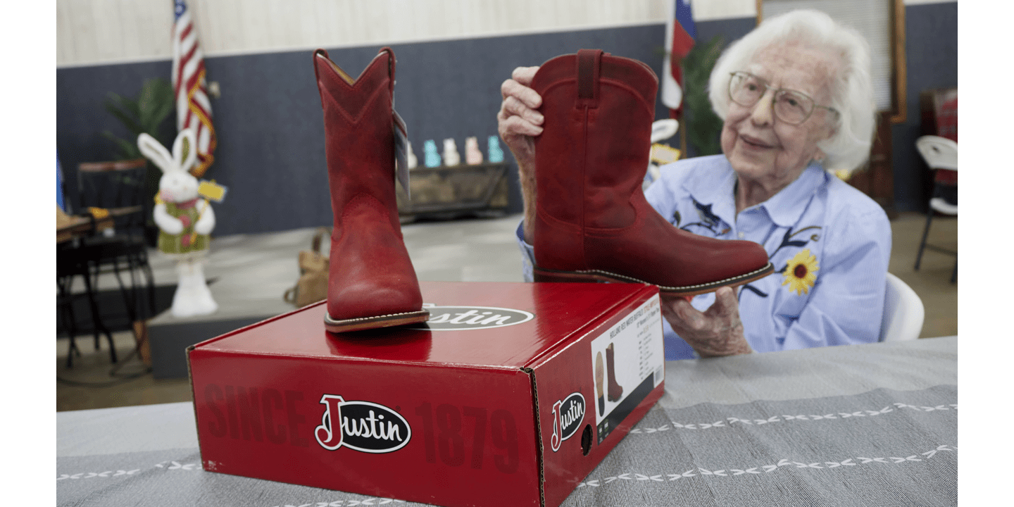 Jean Buford, una señora de cabello gris, gafas y camisa de rayas azules y blancas con flores sosteniendo por primera vez sus flamantes botas rojas roper.